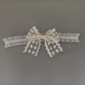 Détail d'un bandeau pour bébé en dentelle blanche avec broderie marguerite et nœud