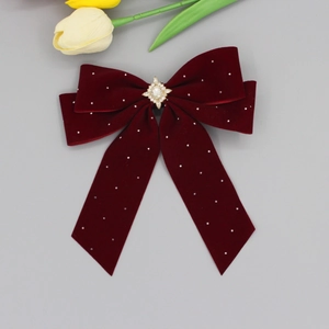Macro view of wine red velvet bow clip with gold crystal center and white rhinestones