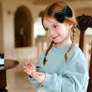 Deep green velvet bow hair clip worn by a young girl in a cozy indoor setting