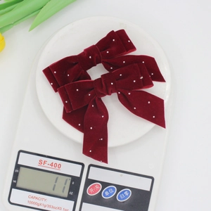 Set of two dark red velvet bow hair clips with rhinestones shown on a digital scale