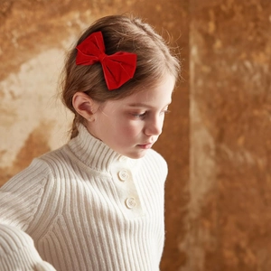 Close-up of a child wearing a red velvet bow hair clip with a classic soft texture