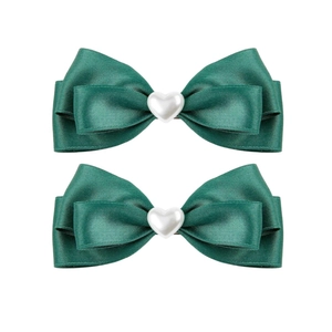 Detail of two dark green satin ribbon hair bows with white heart-shaped pearl centers