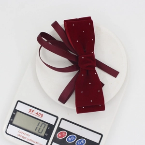 Elegant burgundy velvet bow hair clip with rhinestones shown on a scale weighing 10g