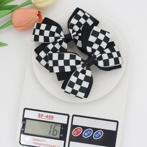 Macro view of black and white checkered bow hair clips being weighed at 16g on a digital scale