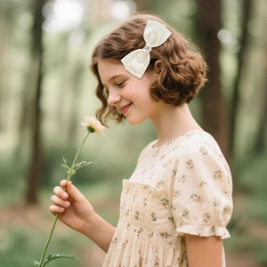 Elegant cream satin ribbon bow hair clip with white pearl center on a girl's hair