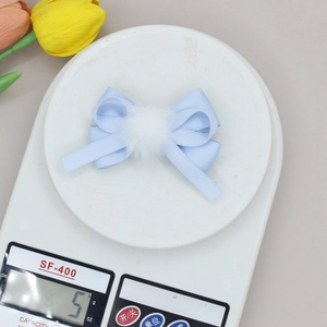 Detail of light blue satin bow hair clip with white pompom on an electronic scale