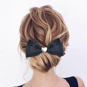 Detail of a black satin bow hair clip with a silver heart center worn on a hair bun