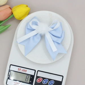 Detail showing the lightweight 8g blue and white bow hair clip with pompom on a scale