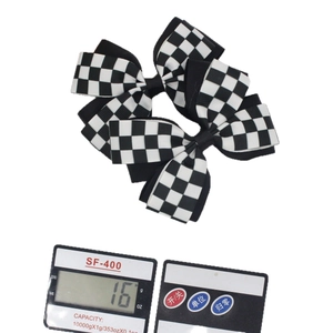 Pair of black and white checkered bow hair clips on a scale weighing 16 grams