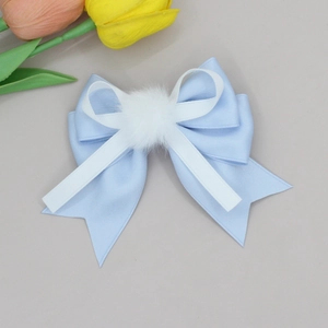 Close-up of sweet blue ribbon bow hair clip with white plush ball detail and satin layers