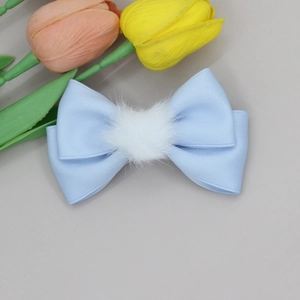 Detail of light blue satin bow hair clip with a white faux fur ball on a clean surface