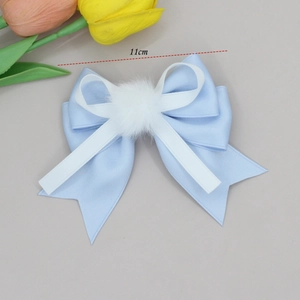 Detail view of 11cm blue satin bow hair clip with white pompom and ribbon accent