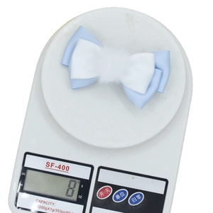 Sweet blue and white bow hair clip with fluffy ball detail on a digital scale