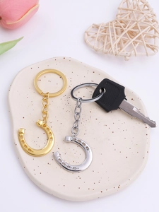 Close-up of polished gold and silver horseshoe keychains on a decorative ceramic tray