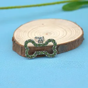 Macro detail of bone-shaped pet charm with green rhinestones on a wooden stand