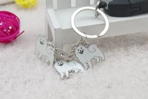 Silver keychain with three white enamel dog charms on a white plush rug with car key