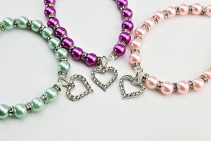Detailed close-up of colorful pearl necklaces with rhinestone heart pendants on white backdrop