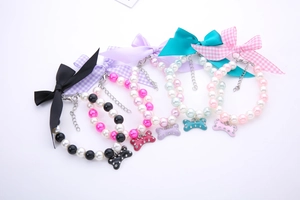 Detailed view of pearl pet collars with ribbon bows and rhinestone bone pendants in five colors