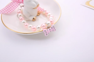 Detail of pink and white faux pearl pet necklace with a rhinestone bone pendant on a plate