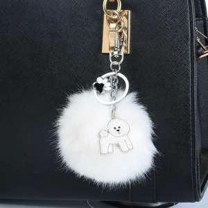 Porte-clés pompon blanc avec pendentif chien et patte attaché à un sac en cuir noir