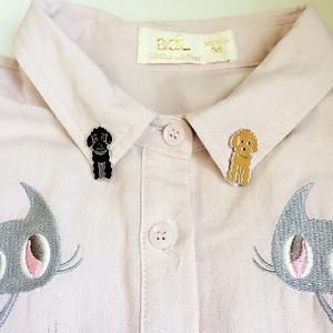 Gros plan de broches en émail de caniches noir et marron sur un col de chemise rose