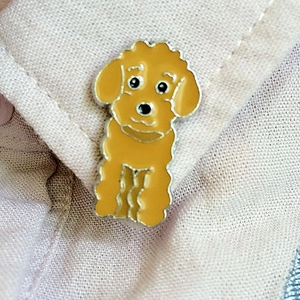Gros plan d'une jolie broche en émail caniche roux fixée sur un tissu rose texturé