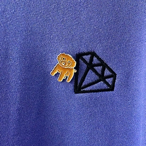 Détail d'une épingle en émail caniche marron sur tissu bleu avec broderie noire