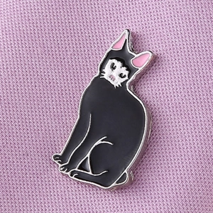 Vue macro d'une broche chat en émail noir avec détails blancs sur tissu rose