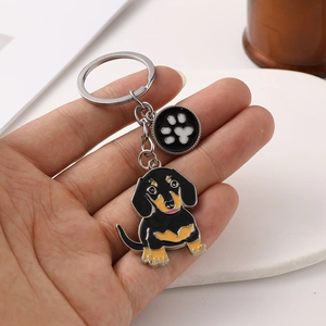 Détail d'un porte-clés teckel avec un charm patte noire tenu dans la main pour taille