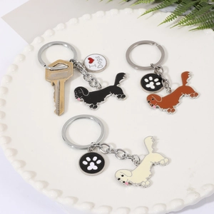 Détails de porte-clés teckel en émail métal en noir, marron et beige sur un plateau blanc