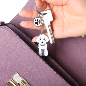 Close-up of white enamel poodle keychain with paw print charm on a purple leather bag