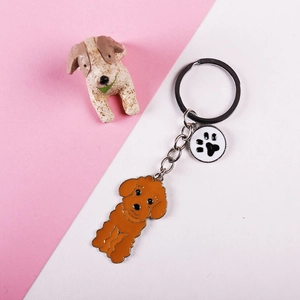 Close-up of orange poodle keychain with black and white paw print charm on metal ring