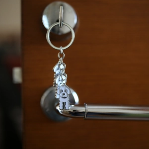Close-up of white enamel poodle keychain with layered metal charms on a door hook