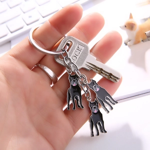 Hand holding a silver metal Jack Russell dog keychain with three black enamel pendants