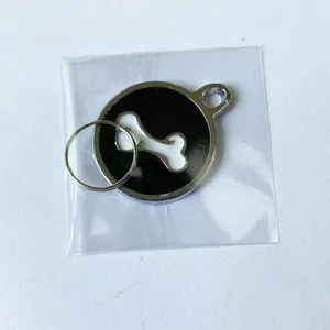 Detail of round black enamel pet tag with white bone motif in plastic packaging