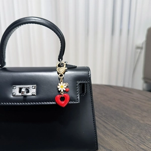 Detail of cute ladybug and daisy keychain charm hanging on a luxury black leather handbag