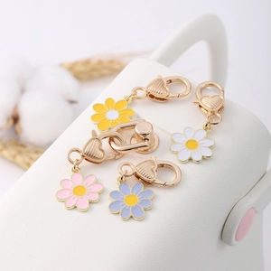 Close-up of enamel daisy flower charms with gold heart clasps on white leather
