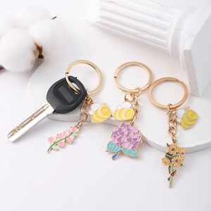 Three-piece bee and flower enamel keychains set with gold rings on white props