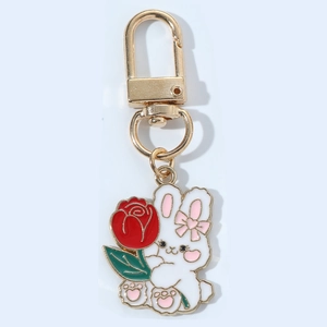 Detail of a white rabbit enamel keychain holding a red rose with golden lobster clasp