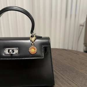 Detail of sunflower enamel charm with golden heart clasp on black leather handbag