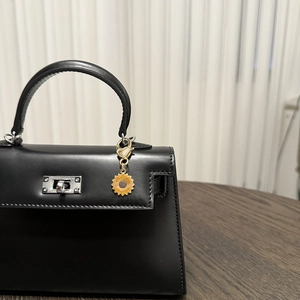 Close-up of golden sunflower pendant charm on black leather Kelly style mini handbag