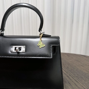 Detail of a black leather Kelly bag featuring silver hardware and a green crystal butterfly charm