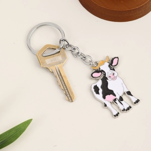 Gros plan d'un mignon porte-clés vache en émail noir et blanc avec anneau doré sur fond beige