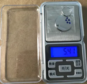 Detailopname van een 25 mm metalen ID-tag met blauwe strassteentjes op een weegschaal van 5,41 g