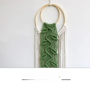 Detail of bohemian woven wall hanging featuring green leaf patterns and white fringe tassels