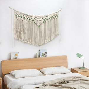 Bohemian woven macrame wall hanging with green beads and tassels above the bedroom bed
