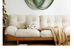 Detailed view of the tufted upholstery and natural wood legs on a cream fabric sofa