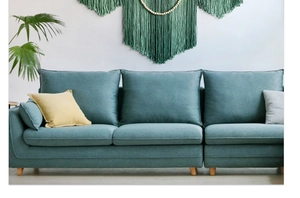 Green handmade woven tapestry with tassels hanging above a modern fabric sofa
