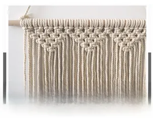Gros plan sur un macramé mural montrant le tissage en coton et la tige en bois naturel