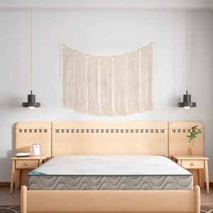 Detail of a beige bohemian woven tapestry on a white wall above a minimalist bed